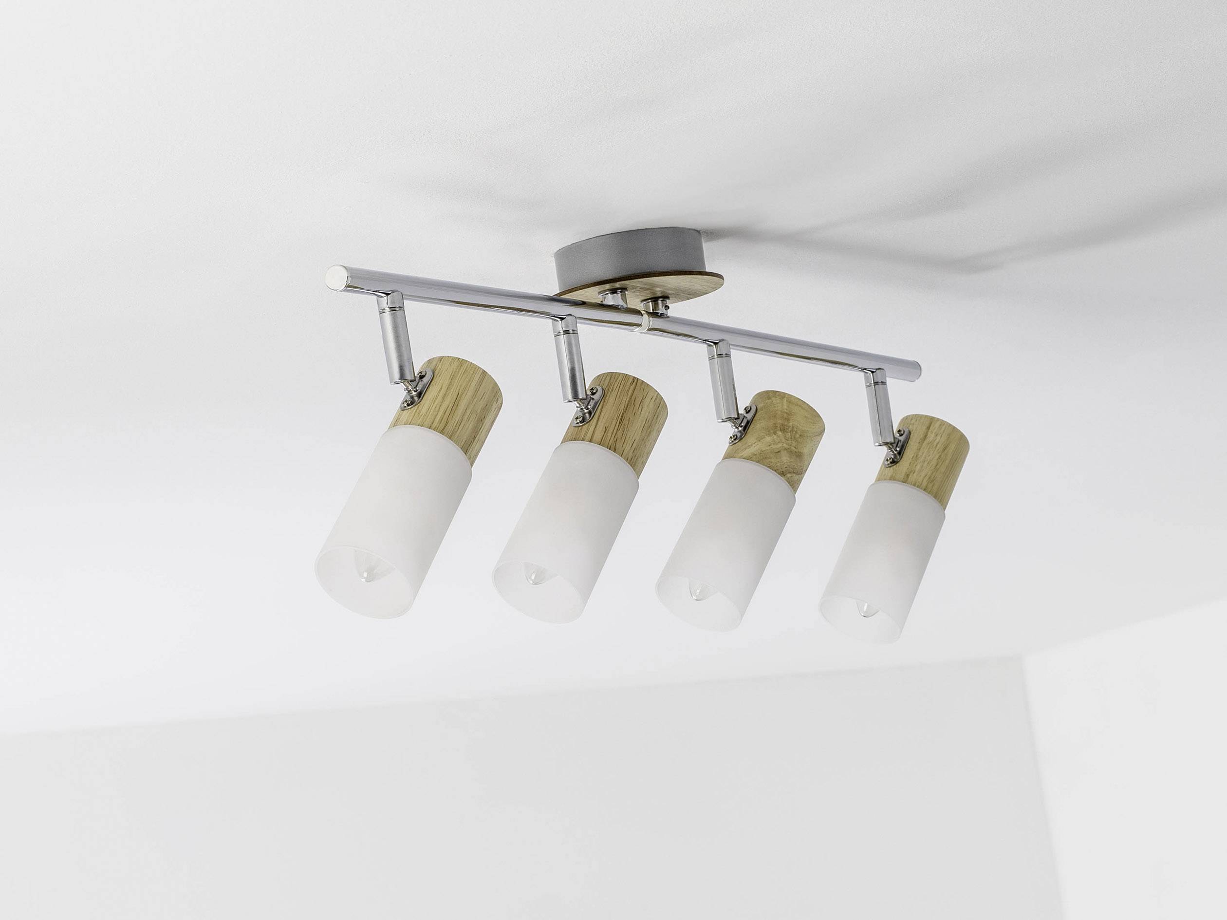Četiri cilindrične stropne lampe na kromiranoj šipki, postavljene na bijelom stropu sobe. Drveni elementi naglašavaju dizajn.