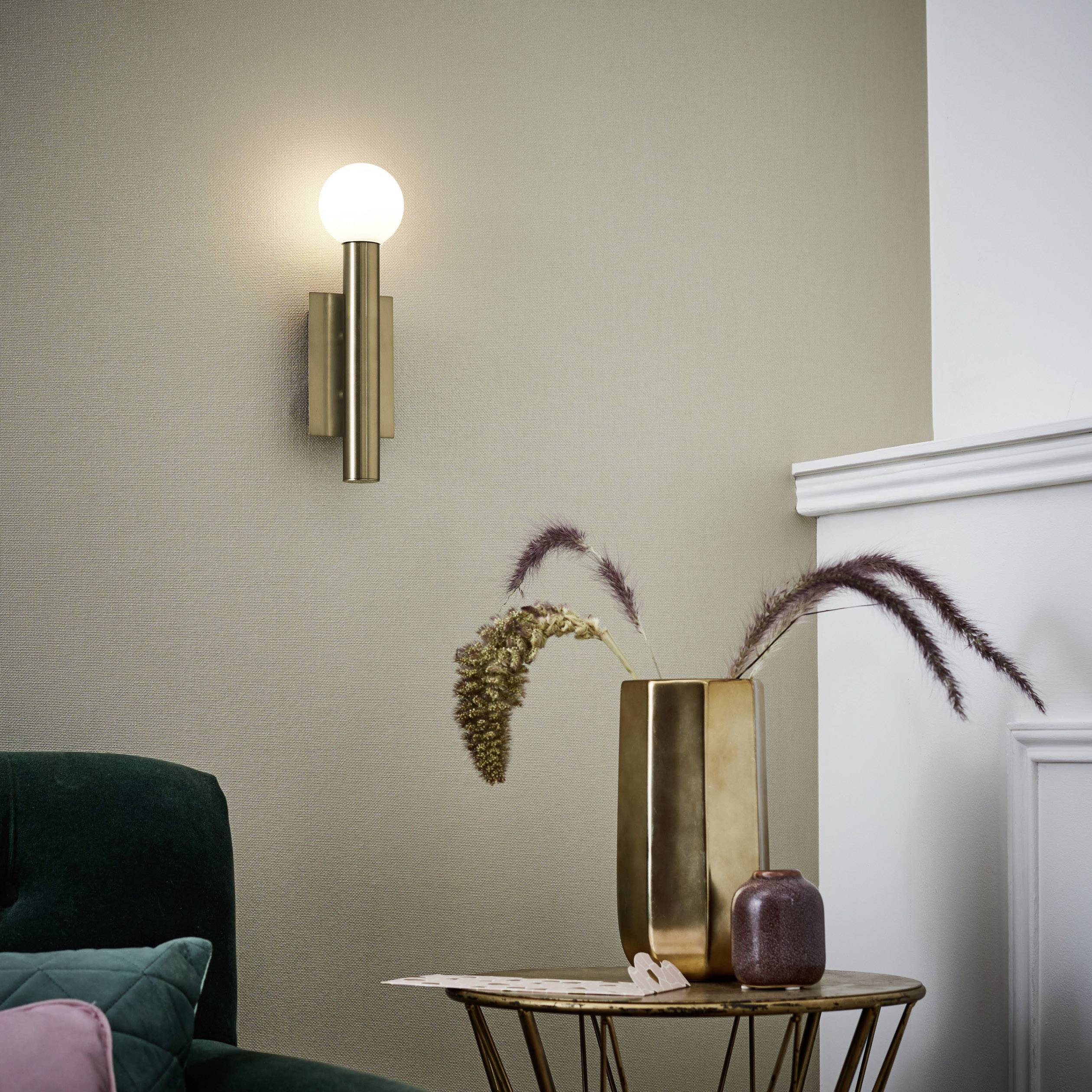 Stilski uređen dnevni boravak s modernom zidnom lampom, zlatnim setom vaza za cvijeće na stolu i zelenom kaučem.