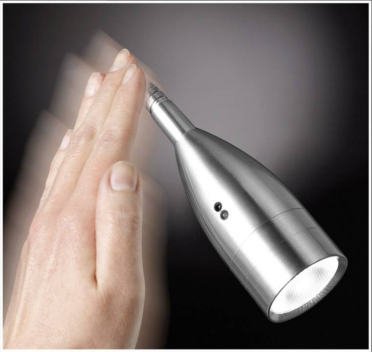 Jedna ruka brzo se pomiče kako bi ugasila futurističku stolnu lampu. Lampa ima vitak, moderan dizajn.