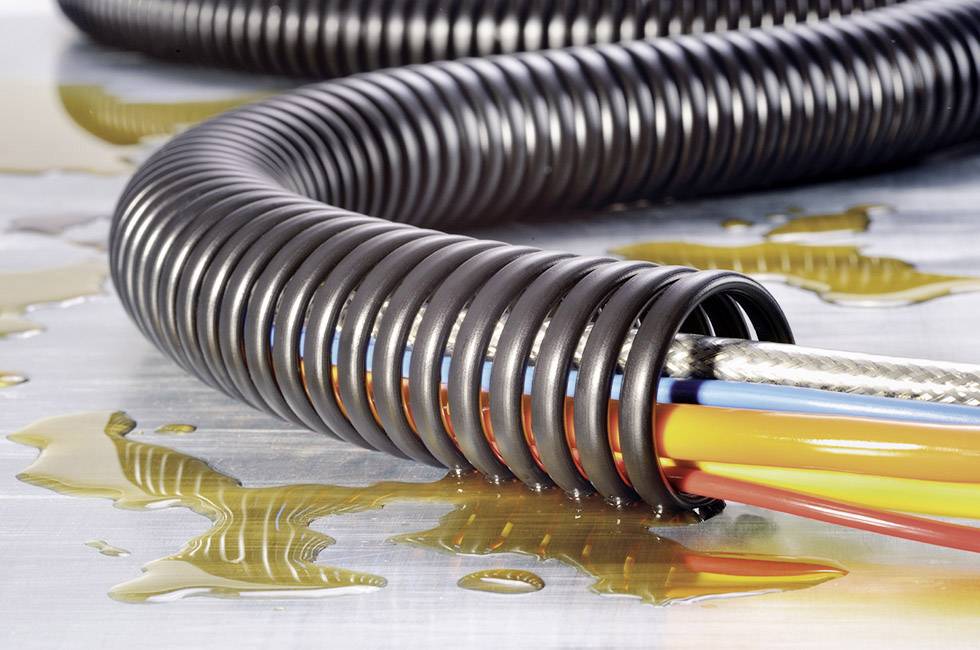 Fleksibilna plastična cijev s više obojenih kabela leži na metalnoj površini prekrivenoj prolivenim uljem.