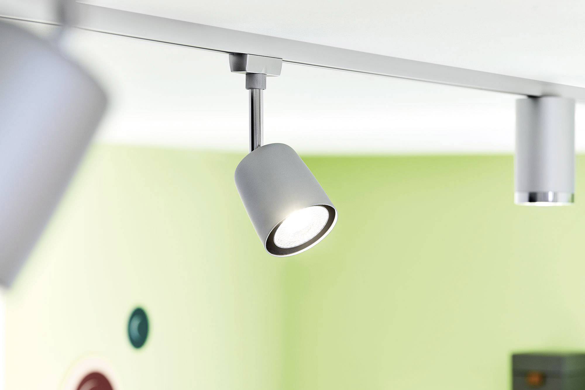 Bijela stropna lampa s tri podesiva reflektora osvjetljava prostoriju sa svijetlozelenim zidom.