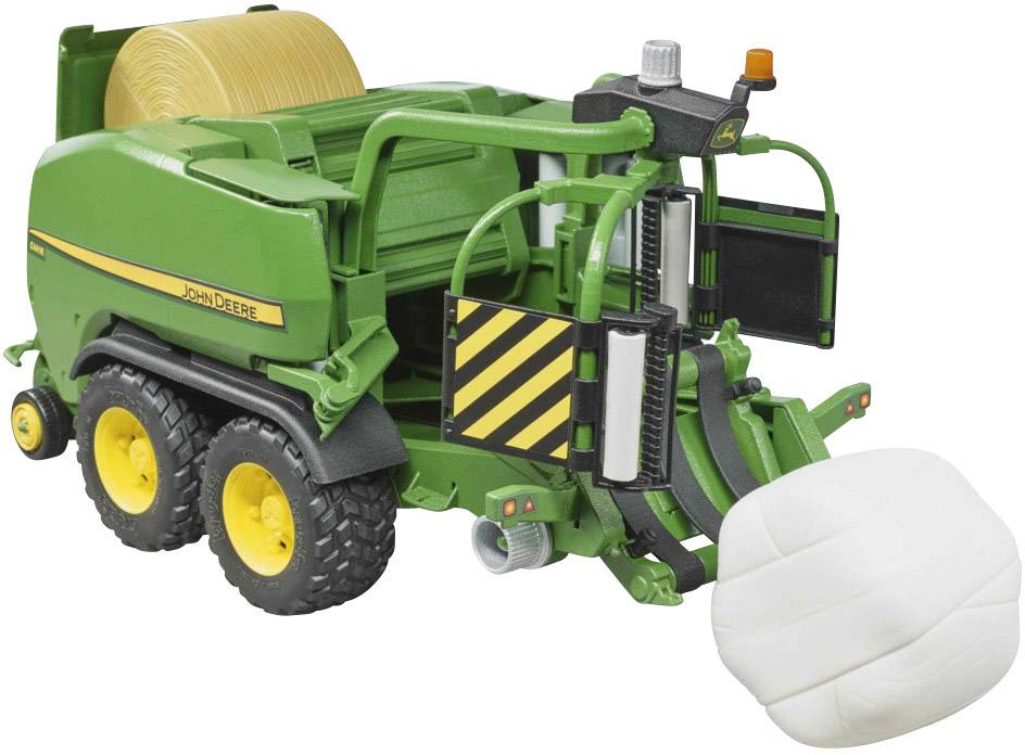 Zeleni igračka traktor sa žutim gumama i balirkom za sjenicu. Bijeli balen sijena leži pored njega na podu.