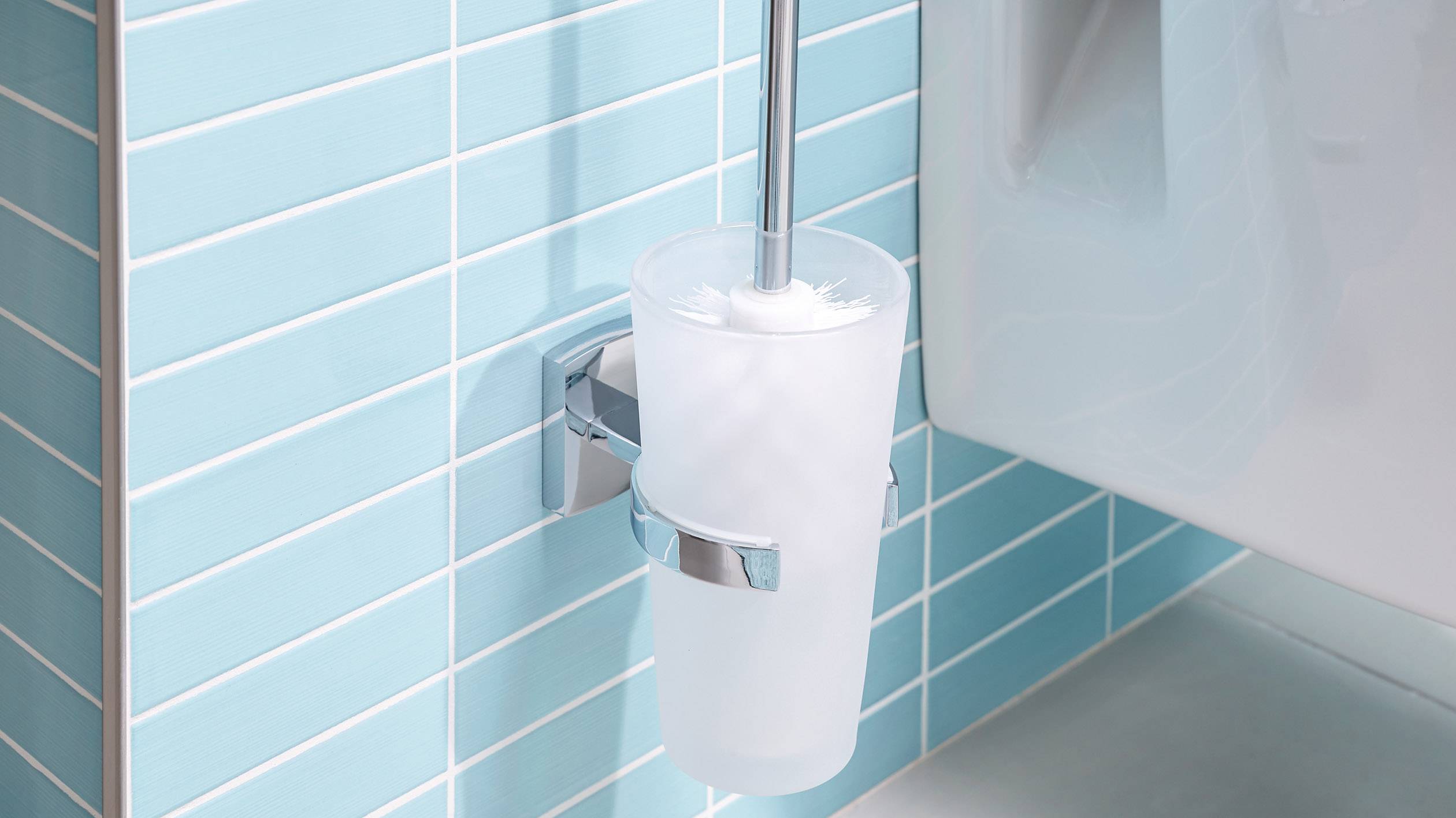 Četka za toaletu u stalku uz plavo pločanu zid kupaone pored bijele WC školjke.
