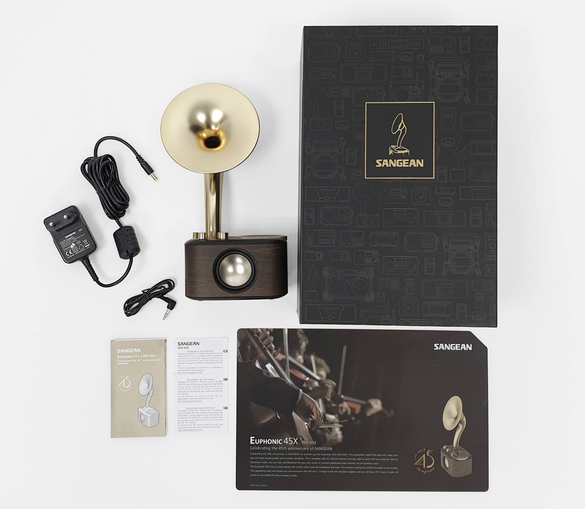 Retro radio s zlatnim zvučničkim lijevkom, pored kojeg se nalaze originalna ambalaža, mrežni adapter i upute. Brand 'Sangean'. Atmosferskog dizajna.