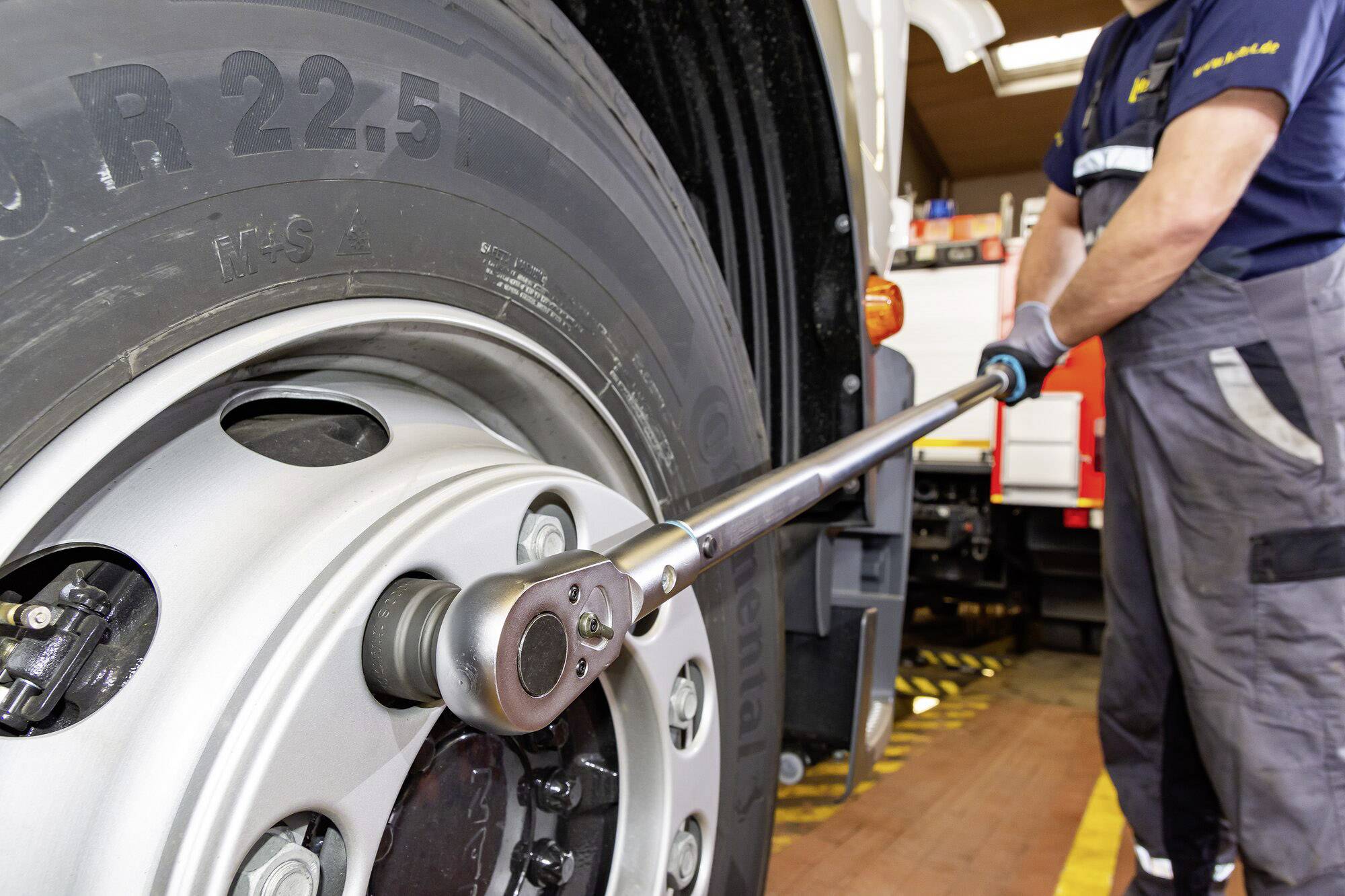 Mehaničar zatežu matice kotača velikog kamionskog gumnog naprava dugačkim ključem u radionici.
