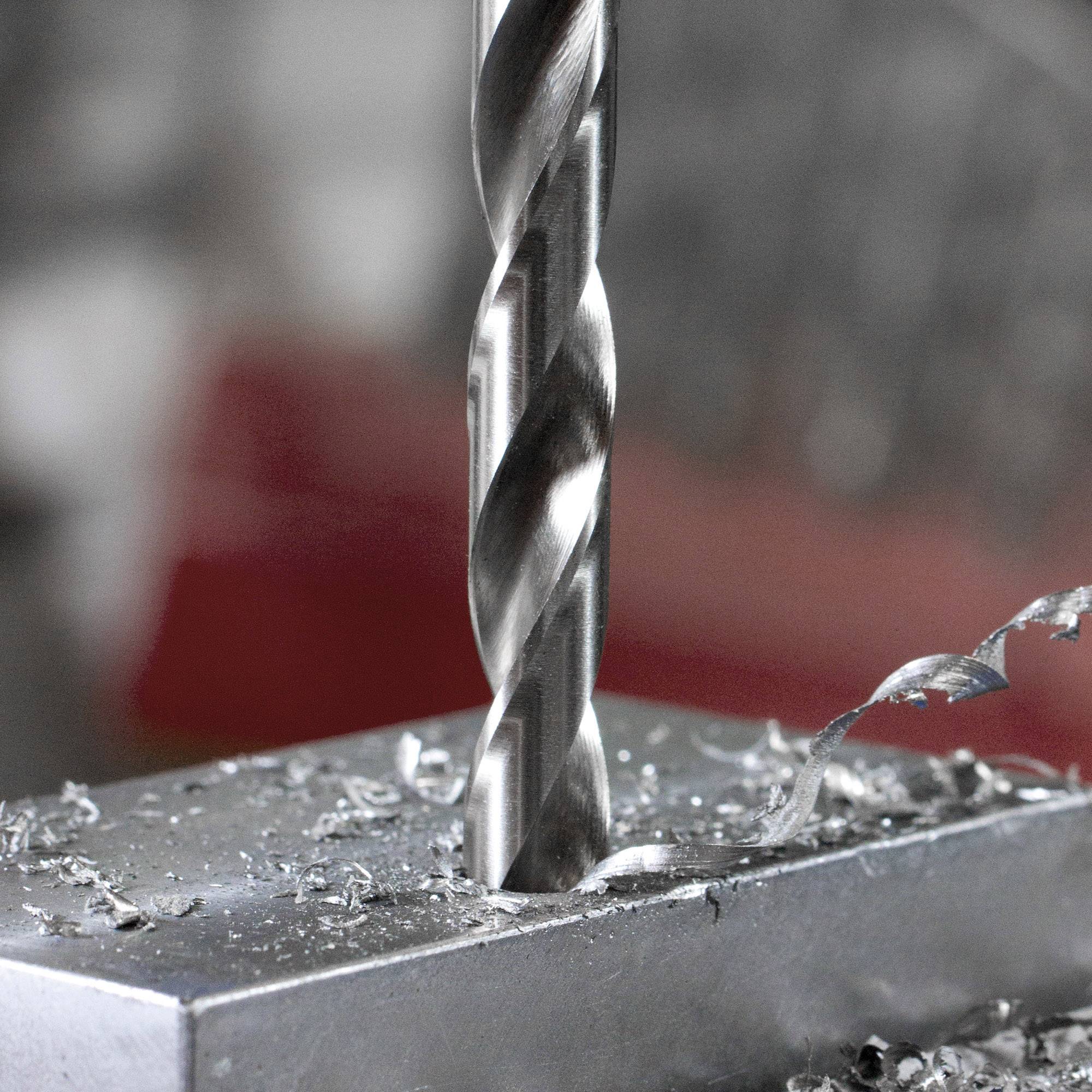 Krupni plan burgije koja buši rupu u komadu metala. Metalne strugotine vidljive su oko rupe, a pozadina je mutna.