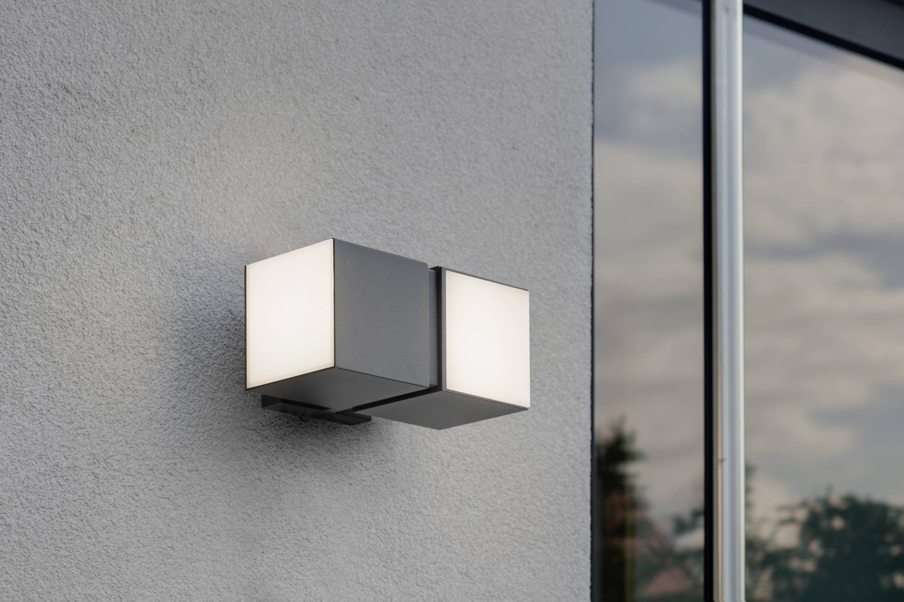 Moderna zidna lampa s pravokutnim kućištem osvjetljava sivo obojani zid pored prozora.