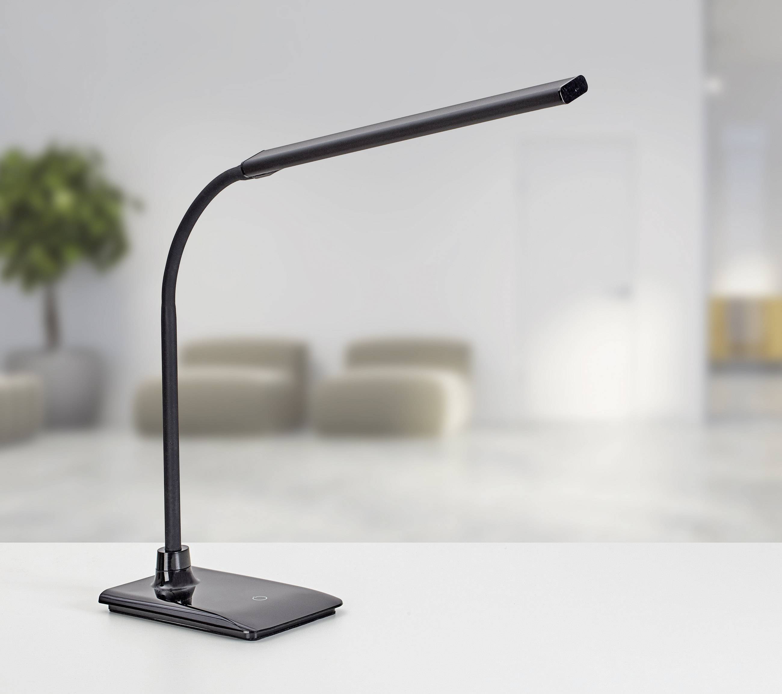 Crna LED stolna lampa s fleksibilnom rukom stoji na bijelom radnom stolu u modernoj, minimalistički uređenoj prostoriji.