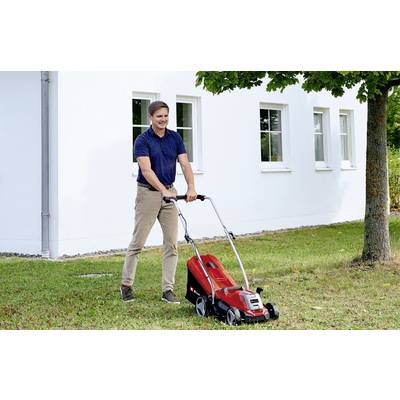 Muškarac kosi travu ispred bijele kuće električnim, crvenim kosilicama. Nebo je plavo, a desno se nalazi stablo.