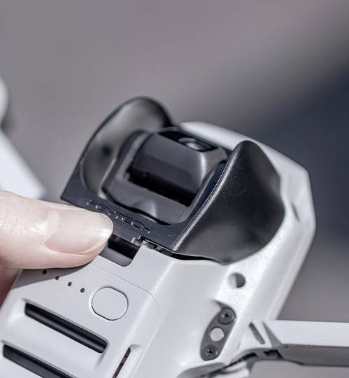 Jedna osoba pažljivo drži dron te dodiruje poklopac kamere, spremna ga možda ukloniti ili prilagoditi.