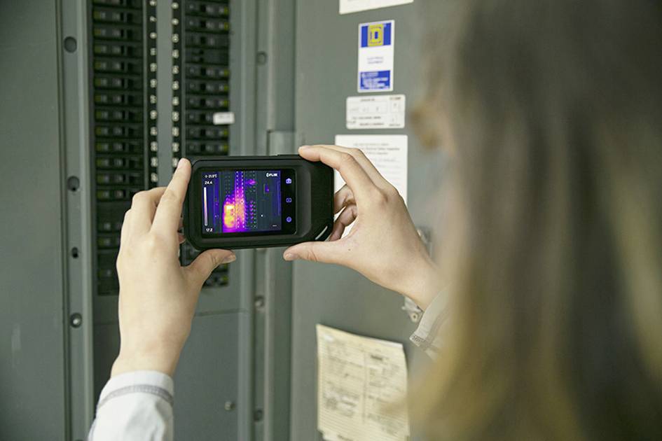 Osoba drži termovizijsku kameru ispred elektro ormara kako bi prepoznala temperaturne razlike. Zaslon prikazuje šarenu termografiju.