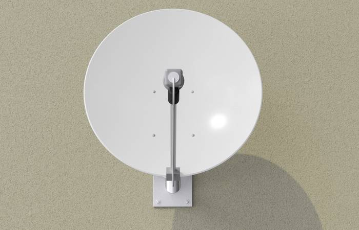 Satelitska antena pričvršćena na zidu, s manjim sjajem koji stvara sunčeva svjetlost.