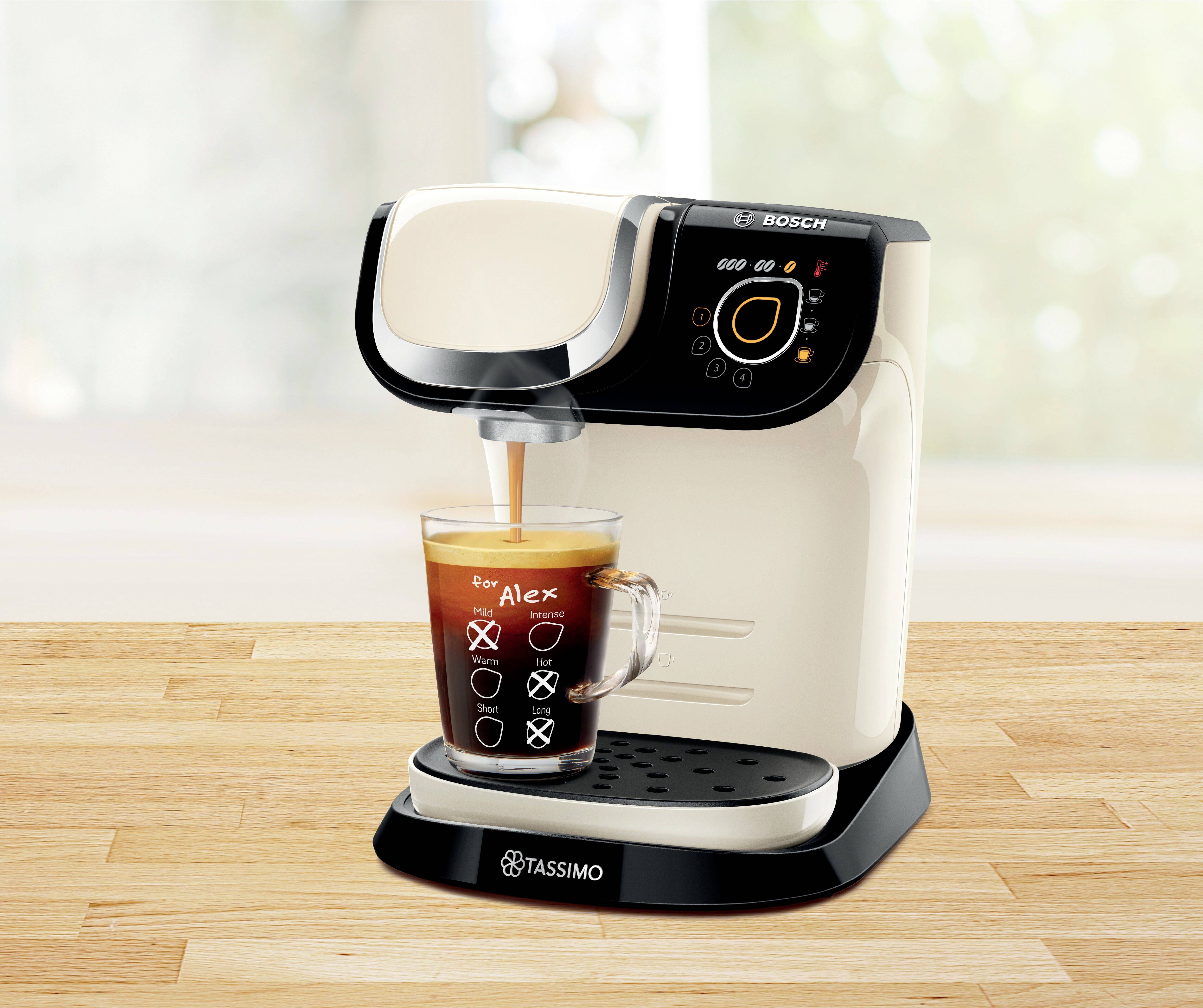 Bijeli Tassimo aparat za kavu tijekom pripreme espresso kave u staklenu šalicu s crnim napitkom. Drvena površina, zamućena pozadina.