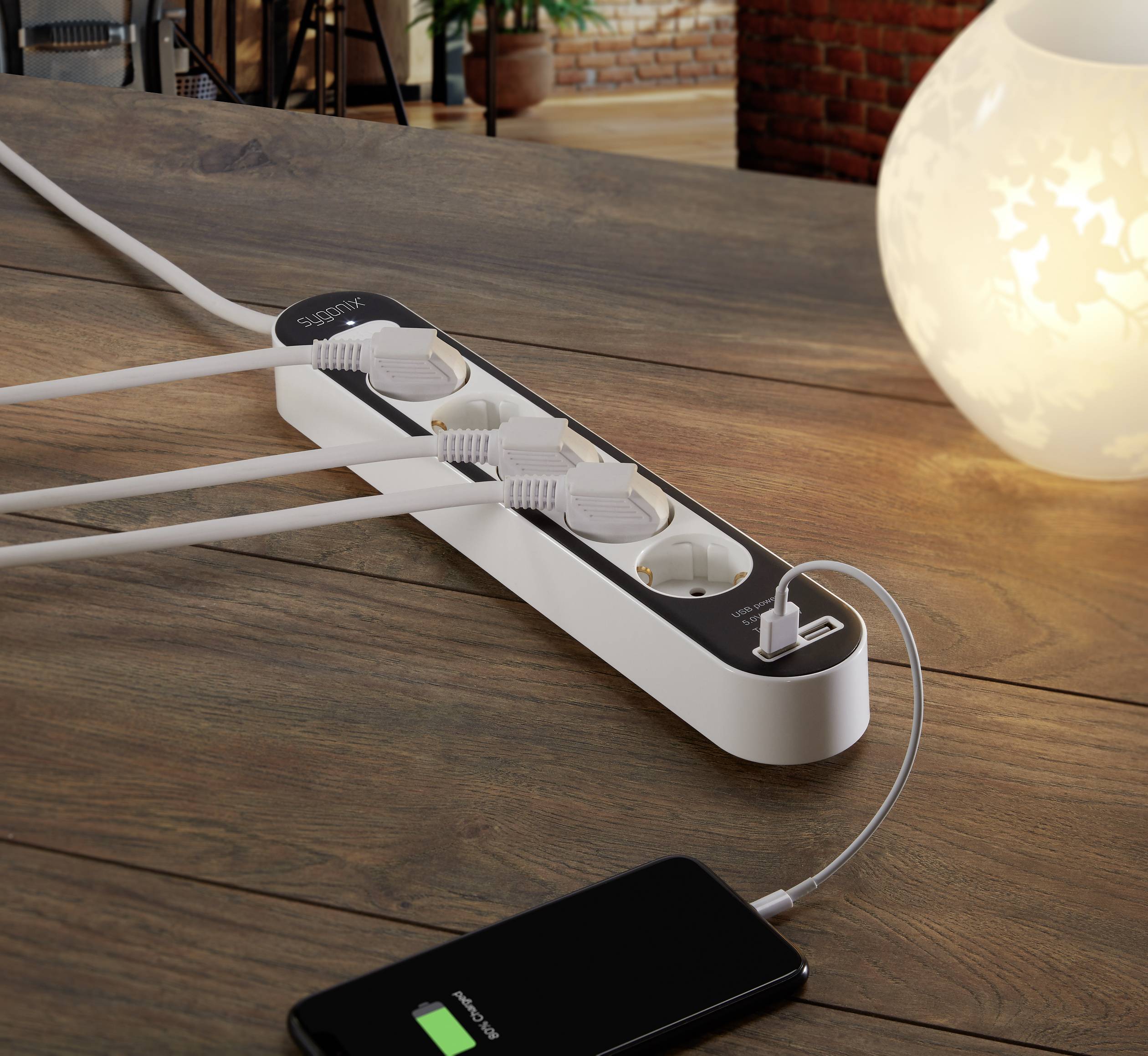 Punjač s više utičnica i USB priključkom punjač je smartphone koji leži na stolu pokraj dekorativne lampe.
