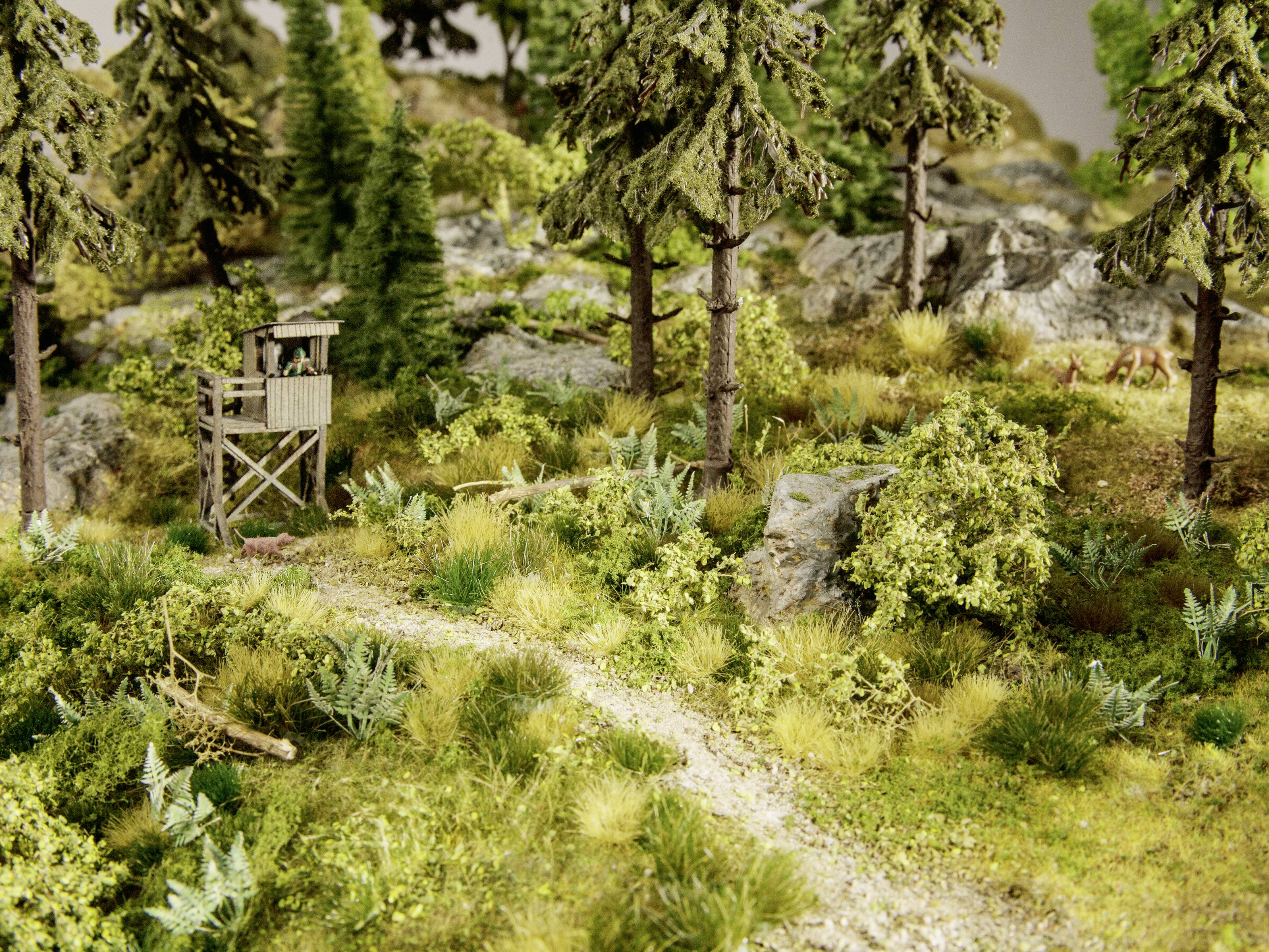 Mini-diorama prikazuje šumu s visokom lovačkom platformom pokraj malog puta, okruženom drvećem i grmljem.