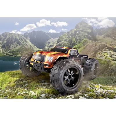Narančasto-crni RC monster truck vozi preko stijenastog terena u planinskom krajoliku. Veliki kotači podižu prašinu.