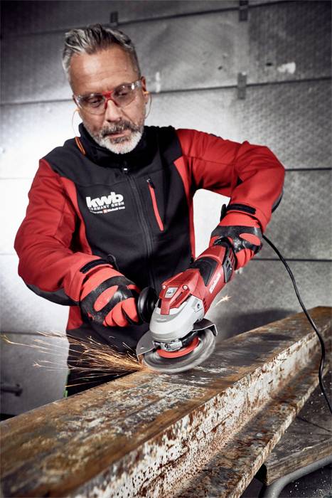 Jedna osoba brusi hrđavi metalni nosač kutnom brusilicom. Varnice prskaju, zaštitna odjeća je na snazi.