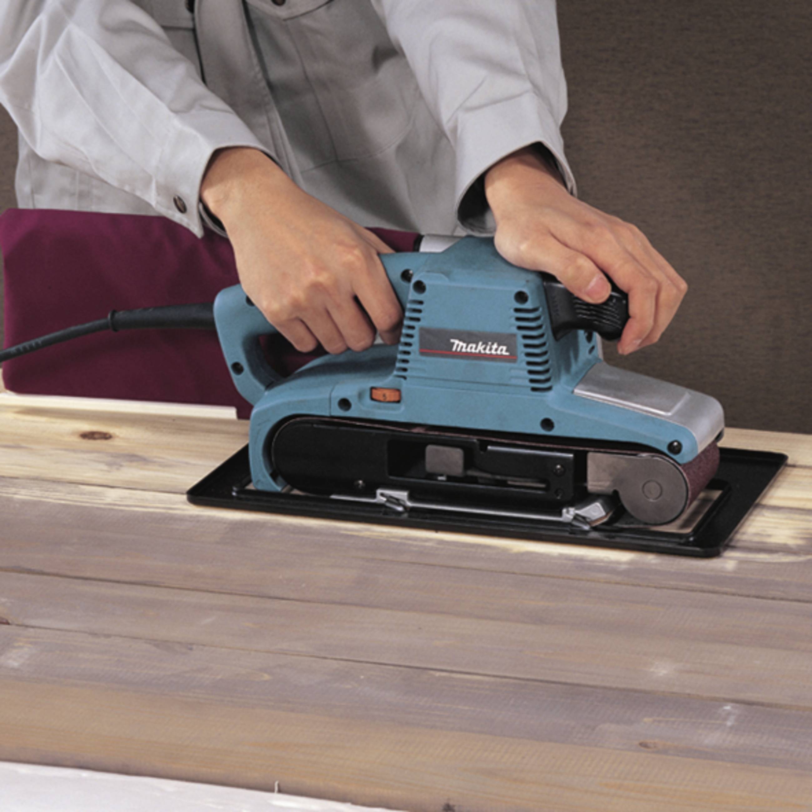 Osoba brusi drvenu ploču električno šlajfericom. Ruke vode uređaj duž površine daske, ostavljajući glatkу strukturu.