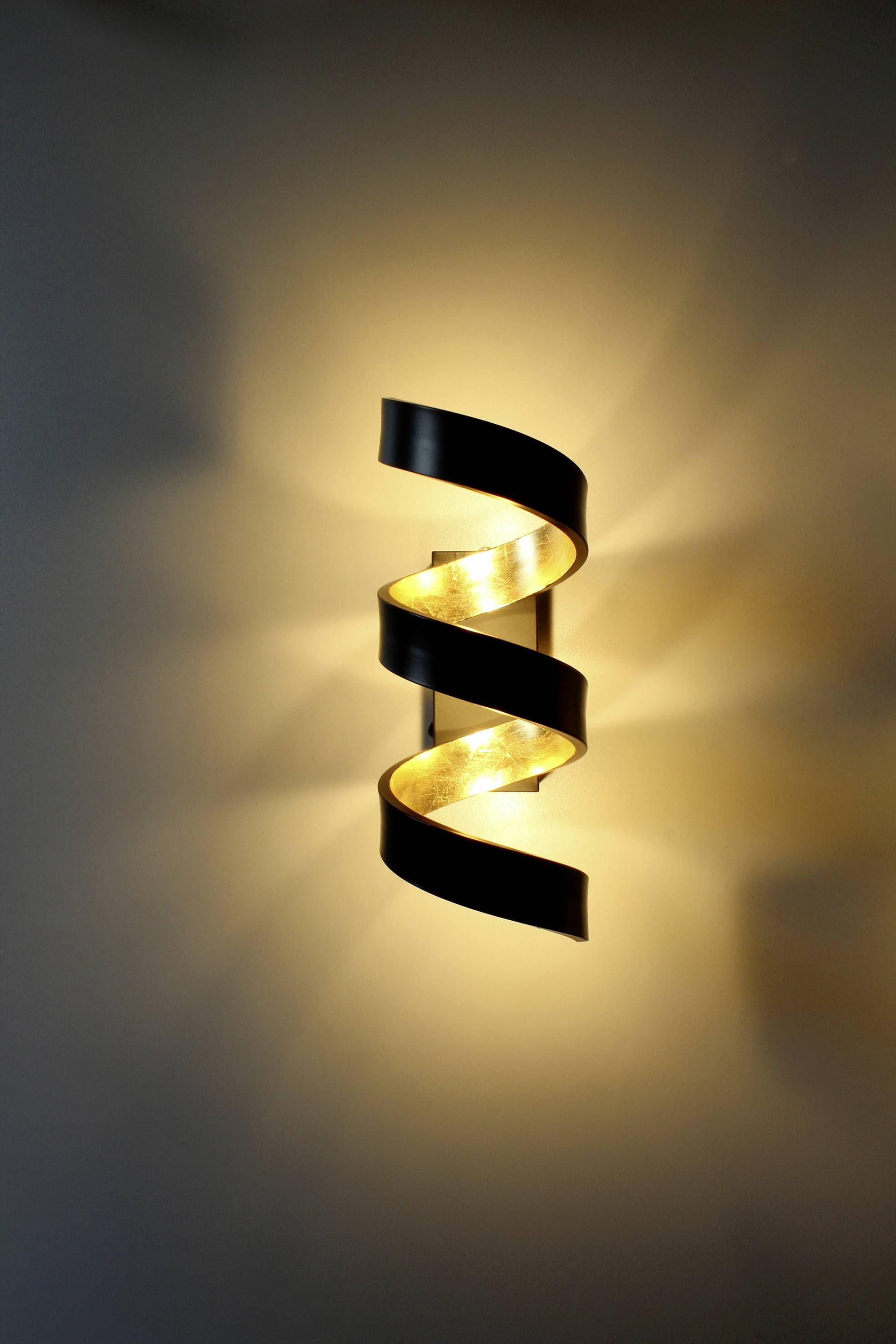 Zidna lampa spiralnog, crnog dizajna koja pruža toplo svjetlo.