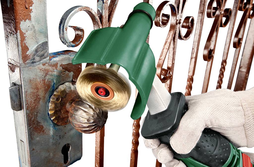 Jedna osoba polira hrđavu metalnu vrata žičanom četkom na električni pogon. Fokus je na čišćenju kvake vrata.