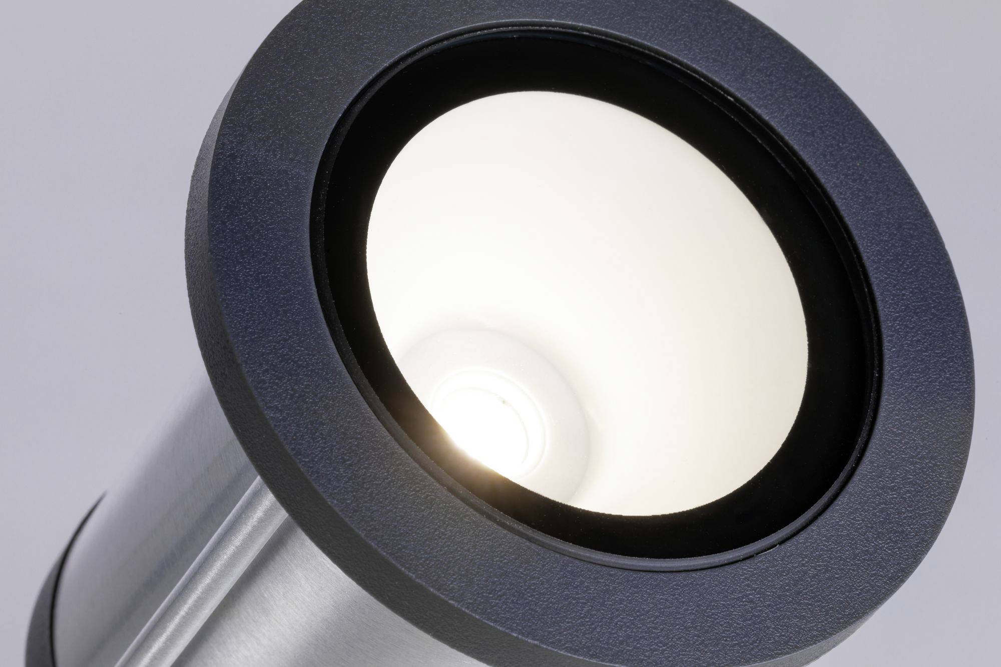 Okrugla srebrna vanjska lampa sjaji bliješteći na sivoj pozadini.