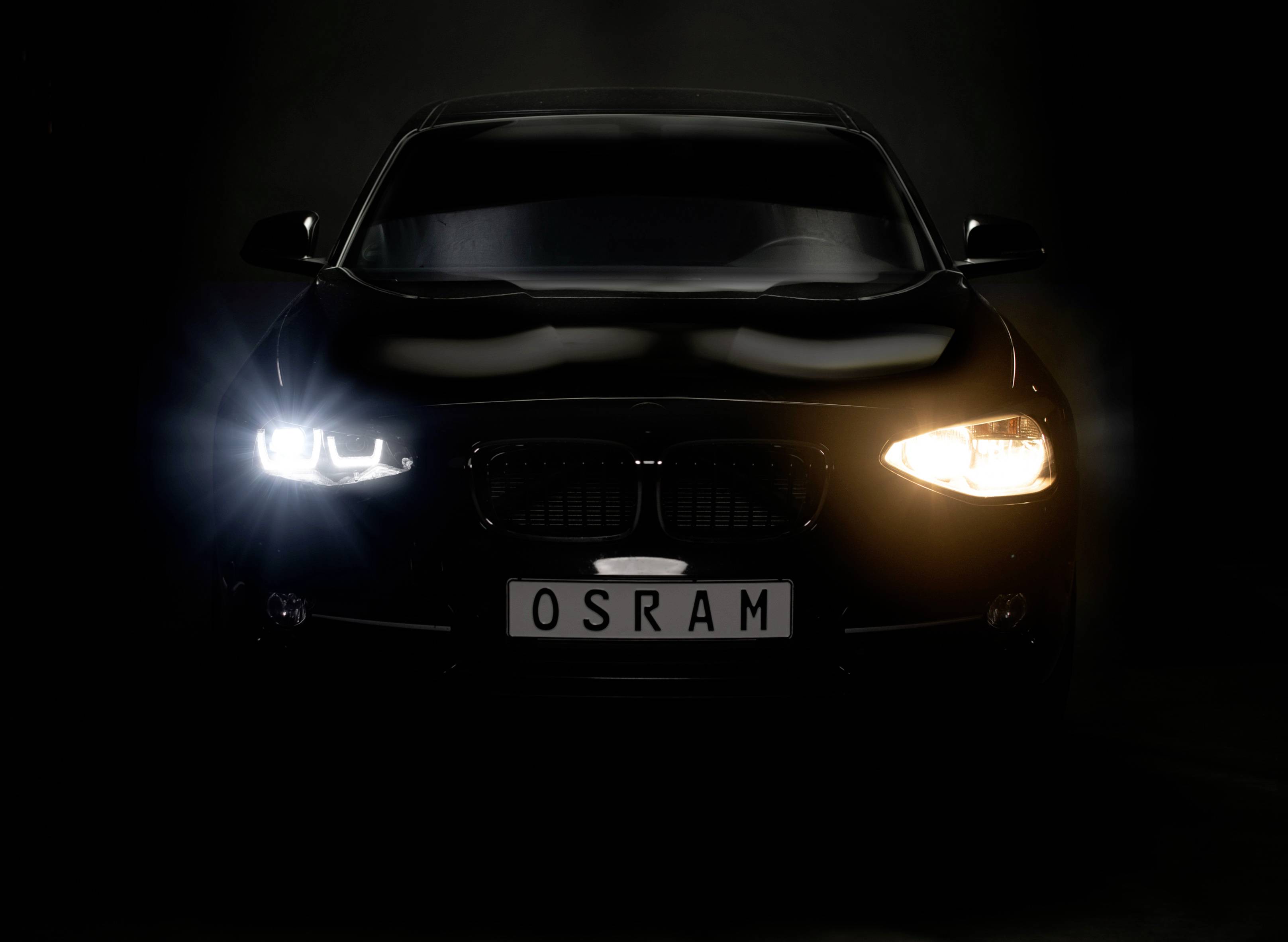 Automobil s osvjetljenim farovima i OSRAM registarskom tablom stoji u mračnom okruženju, naglasak na funkcionalnosti farova.