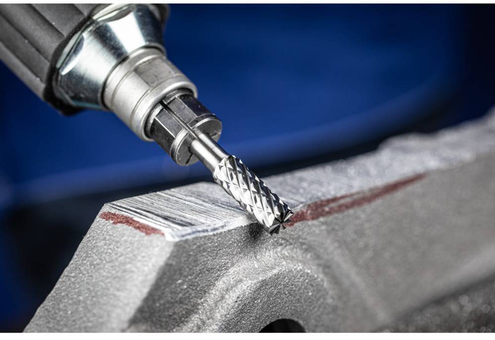 Krupni plan kutne brusilice koja brusi metal. Površina prikazuje tragove brušenja. U pozadini nejasno plavo.