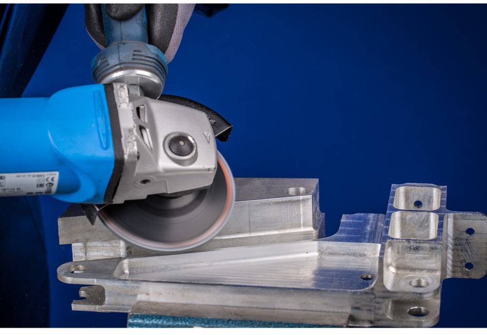 Radnik brusi komad metala plavom brusilicom. Podczas obrade metala nastaju iskre i strugotine.