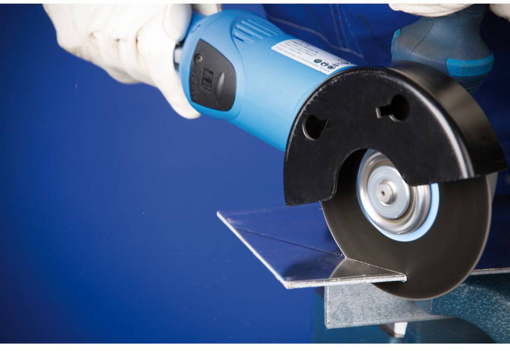 Električna kutna brusilica reže komad metala. Osoba nosi bijele zaštitne rukavice i sigurno drži alat.