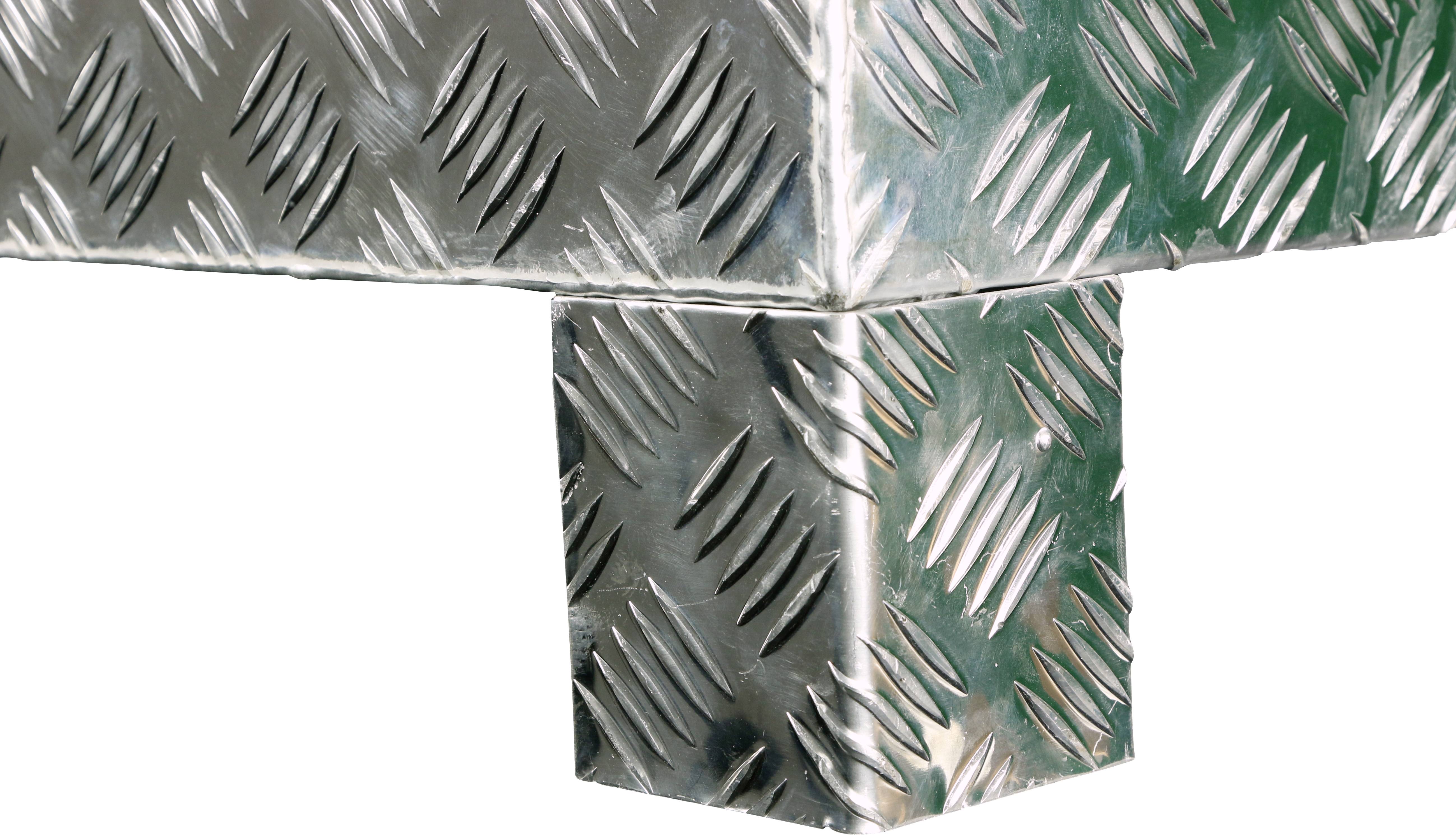 Bliski kadar dijela metalnog stola od čeličnog lima s rebrima. Prikazuje tipičan, paralelni uzorak povišenih ureza na površini.