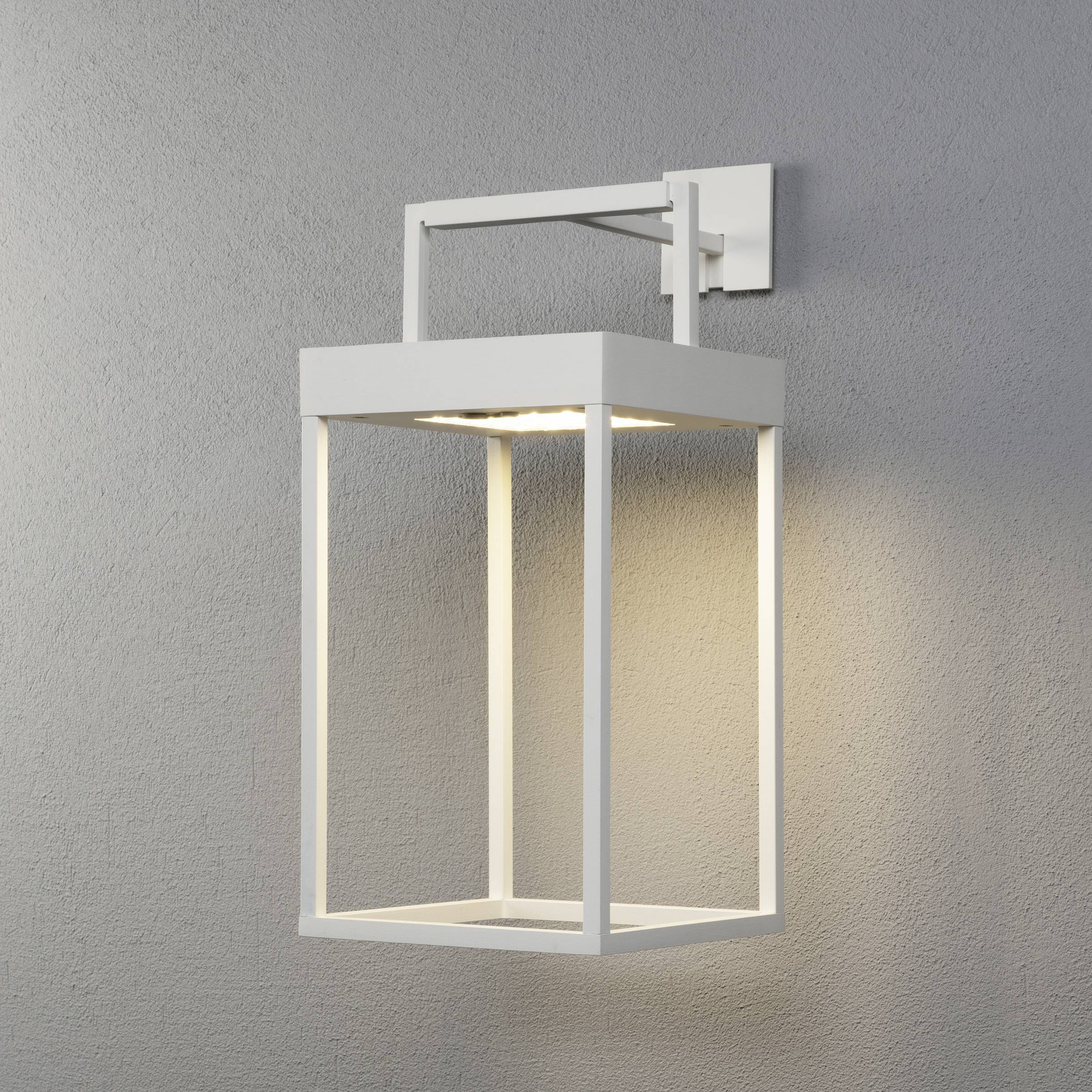 Bijela, moderna zidna lampa minimalistički dizajnirana, pričvršćena na sivi zid. Svjetlo se širi prema dolje i bočno.