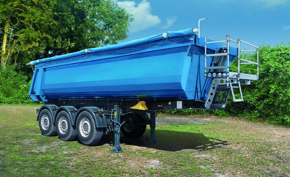 Plavi prikolica s tri kotača stoji na livadi, okružena drvećem i grmljem. Nebo je vedro i plavo.