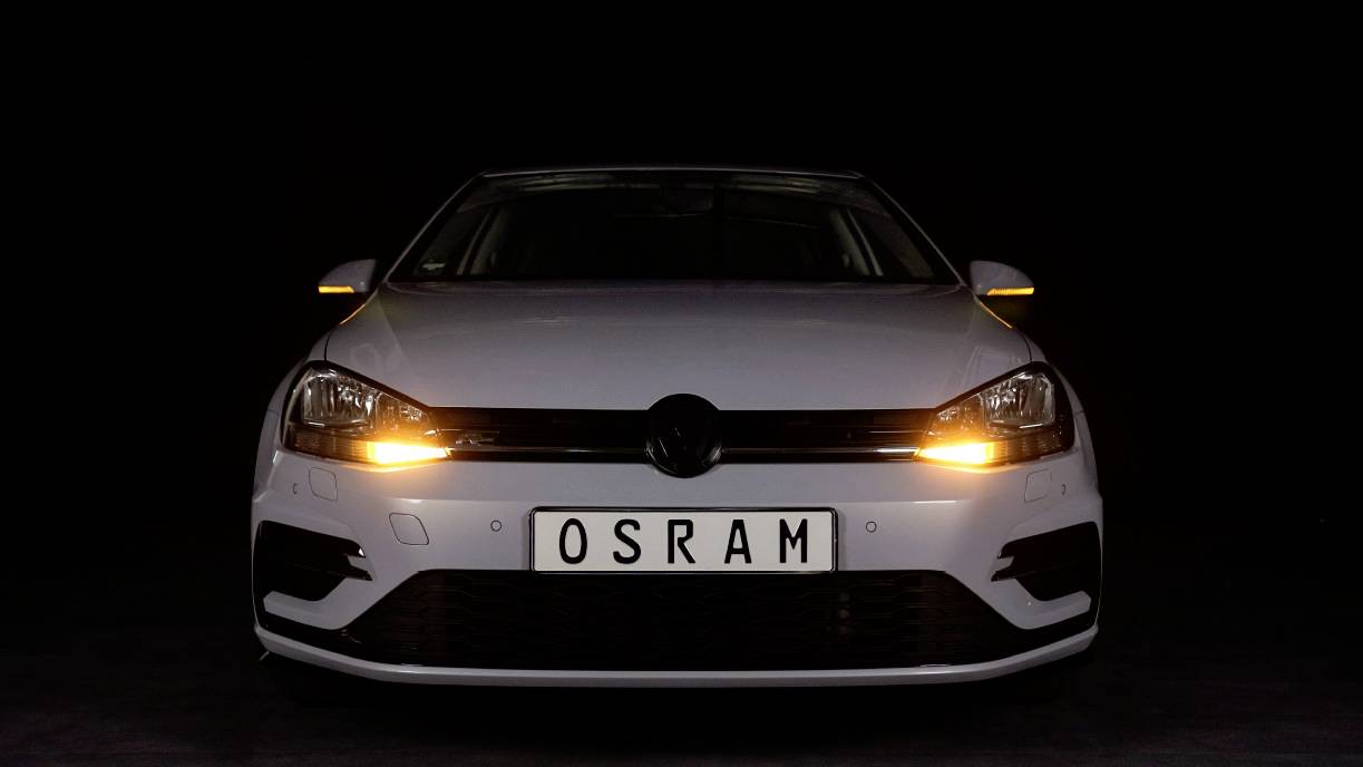 Bijeli automobil s uključenim pozicijskim svjetlom na tamnoj pozadini. Registarska tablica pokazuje 'OSRAM'.