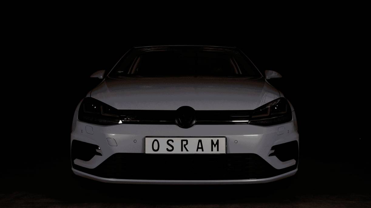 Automobil s uključenim farovima u mraku, registracijska tablica 'OSRAM', farski su istaknuti na crnoj pozadini.