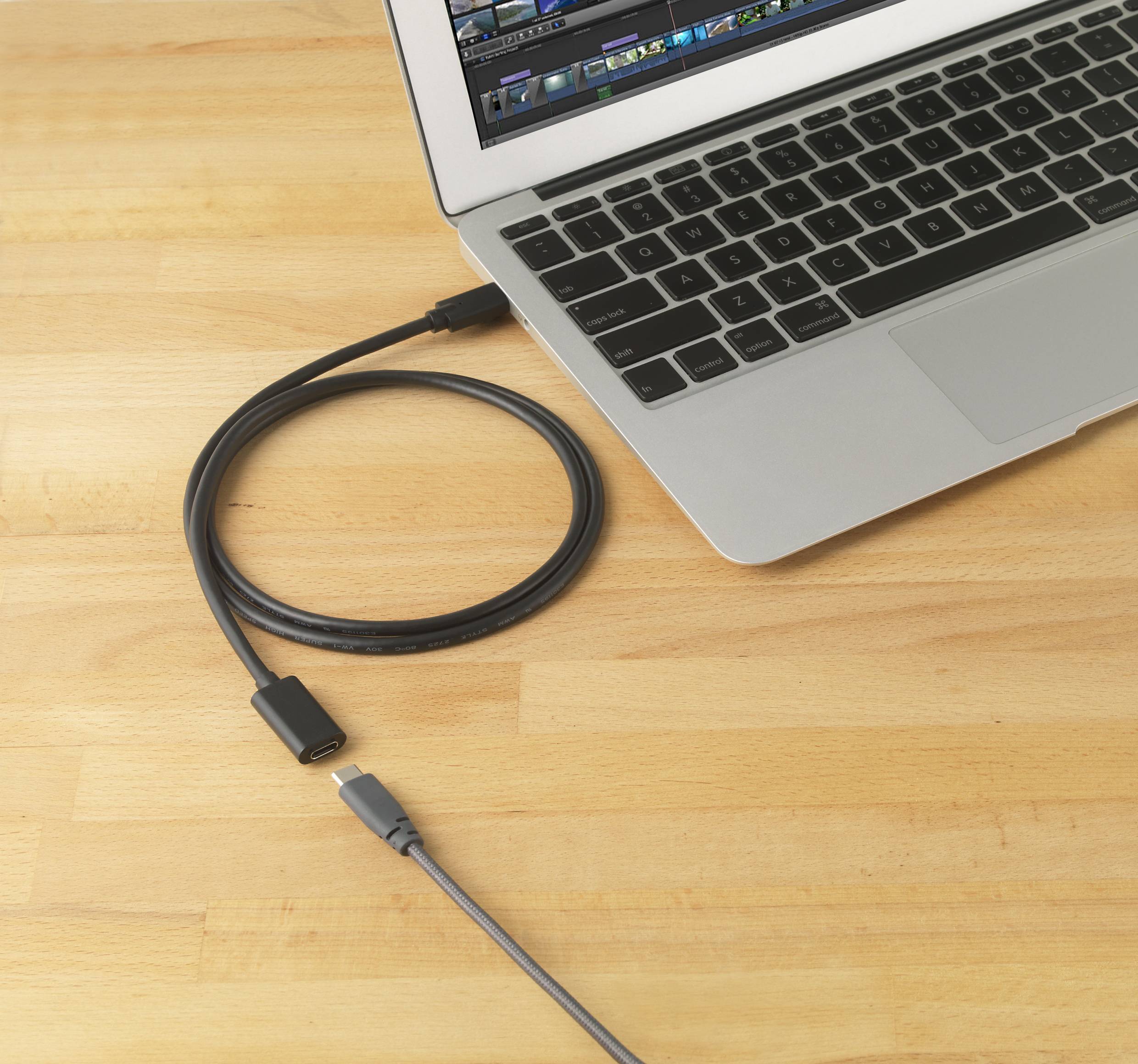 Prijenosno računalo na drvenom stolu s programom za uređivanje slika na zaslonu. Pored njega leži USB-C kabel.