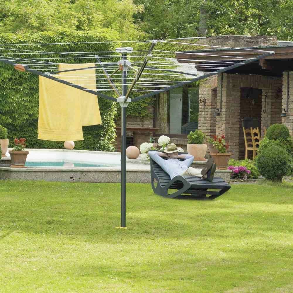 Osoba se opušta na ležaljci u vrtu, pokraj bazena i stalka za sušenje rublja s obješenim ručnikom; sunčana atmosfera.