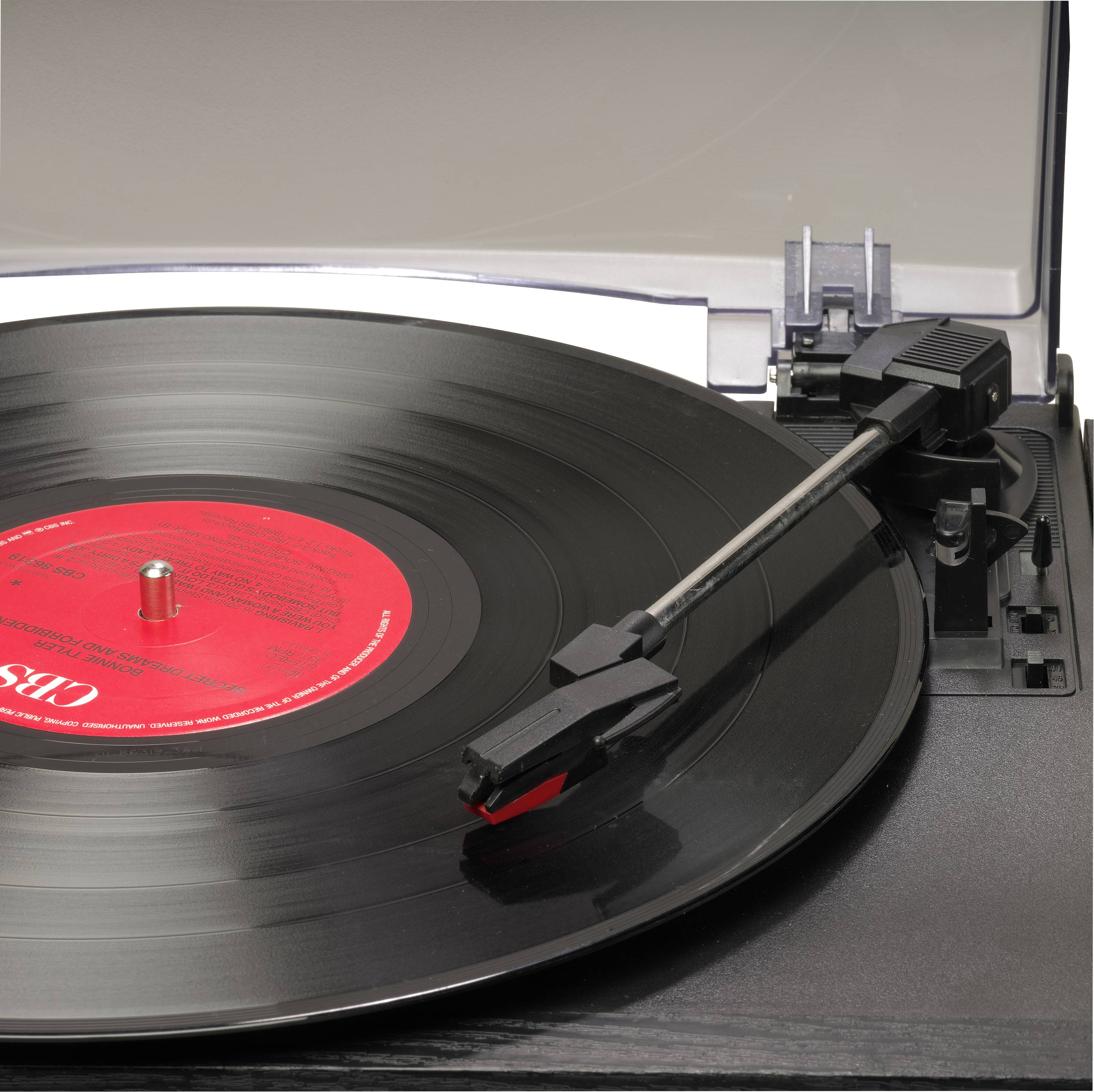 Gramofon s crnom gramofonskom ploča, tonski priključak je postavljen iznad ploče, spreman za reprodukciju. U pozadini prozirni poklopac.