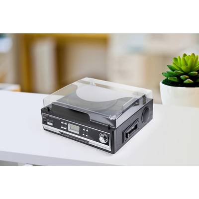 Gramofon s prozirnim poklopcem stoji na stolu. U pozadini se vidi zelena biljka.