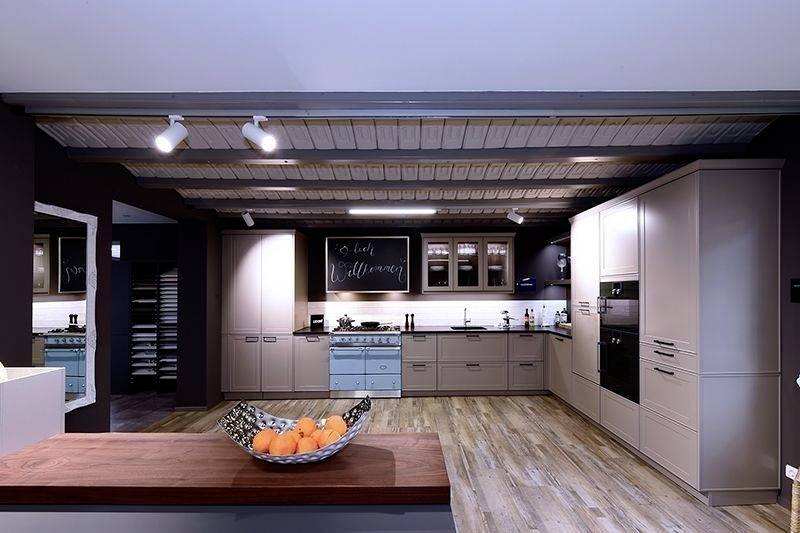 Moderna kuhinja s drvenim podom, bijelim ormarićima i središnjim otokom. Na zidu visi ploča na kojoj piše 'Dobrodošli'.