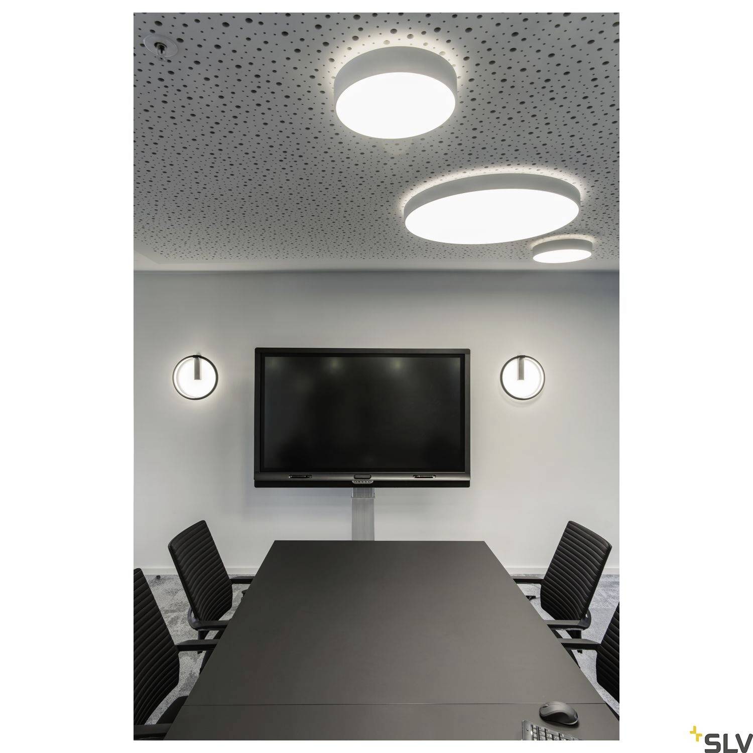 Konferencijska sala s dugačkom stolnom pločom, stolcima i zidnim monitorom. Okrugla stropna i zidna rasvjeta osvjetljavaju prostoriju.