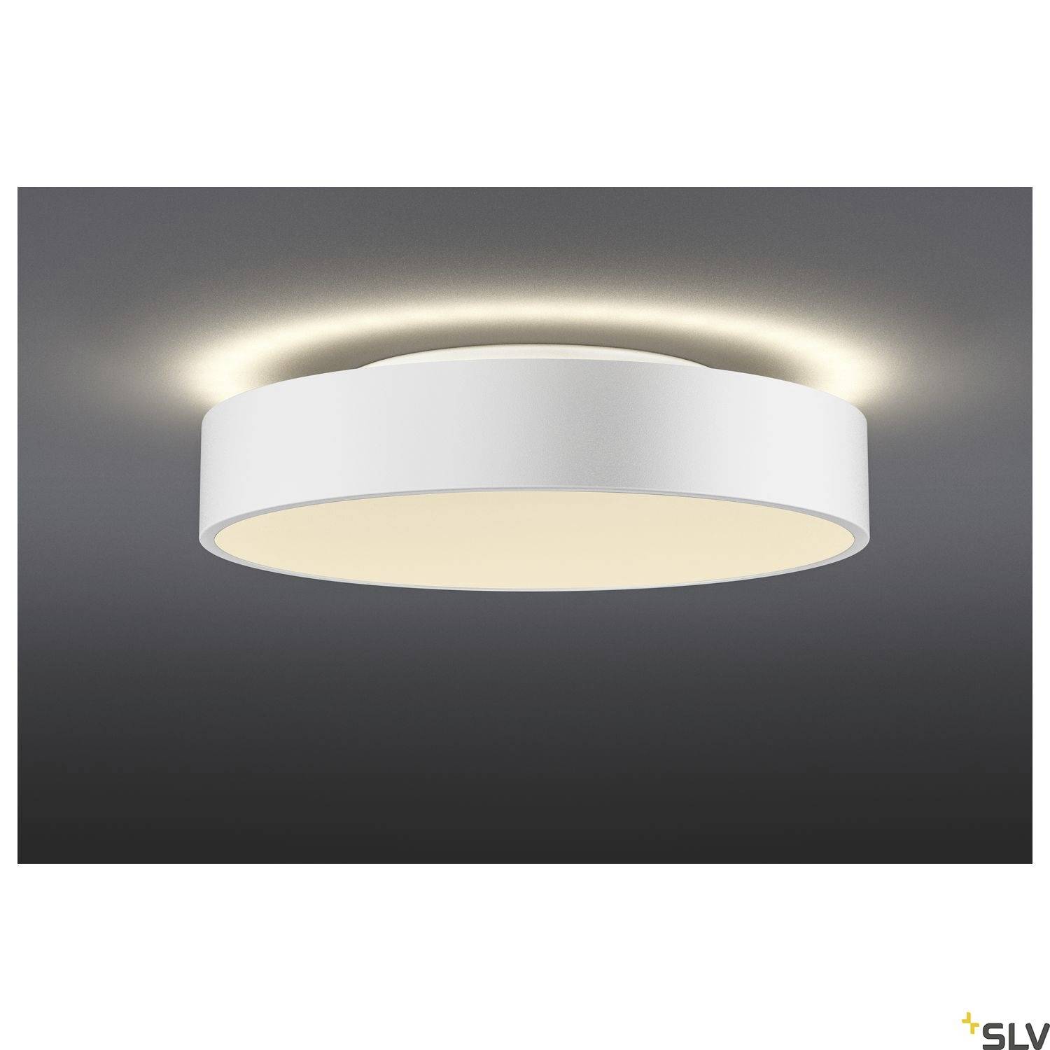 Okrugla, bijela stropna lampa odašilje toplo, indirektno svjetlo te stvara sjajan, kružni halo na stropu.