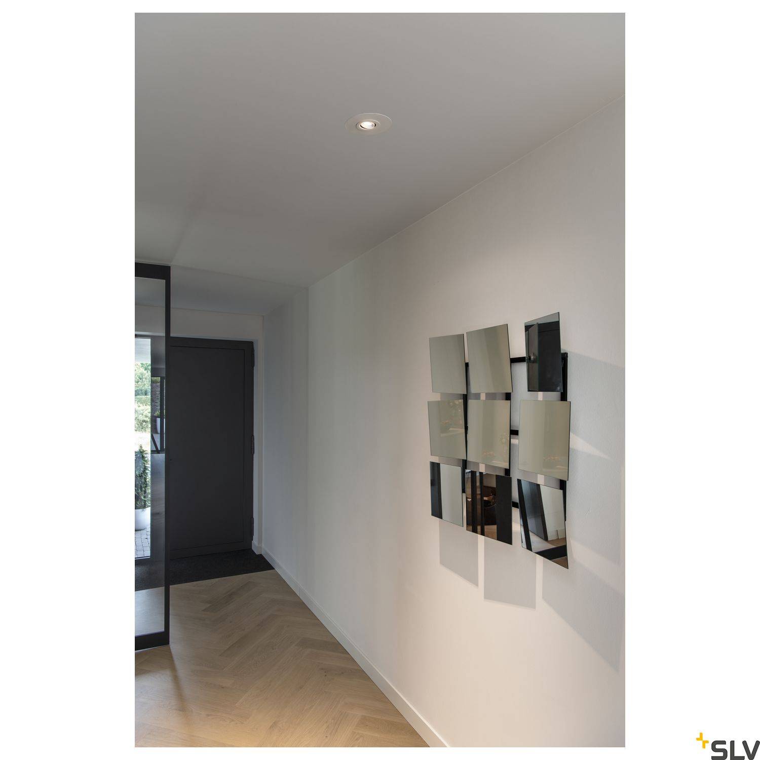 Prazan moderan hodnik sa zrcalom na desnoj stijeni i drvenim podom. S lijeve strane vidljiva je staklena vrata.