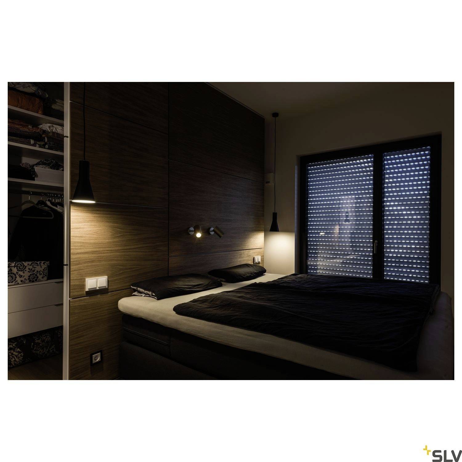 Tamna spavaća soba sa zatvorenim prozorom, bračnim krevetom, dvije zidne lampe i ormar s otvorenim policama.