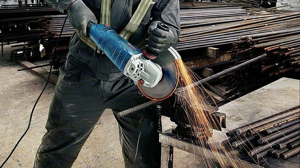 Jedna osoba reže čelične šipke kutnom brusilicom. Varnice lete s mjesta kontakta. Radi se o radioničkom okruženju.