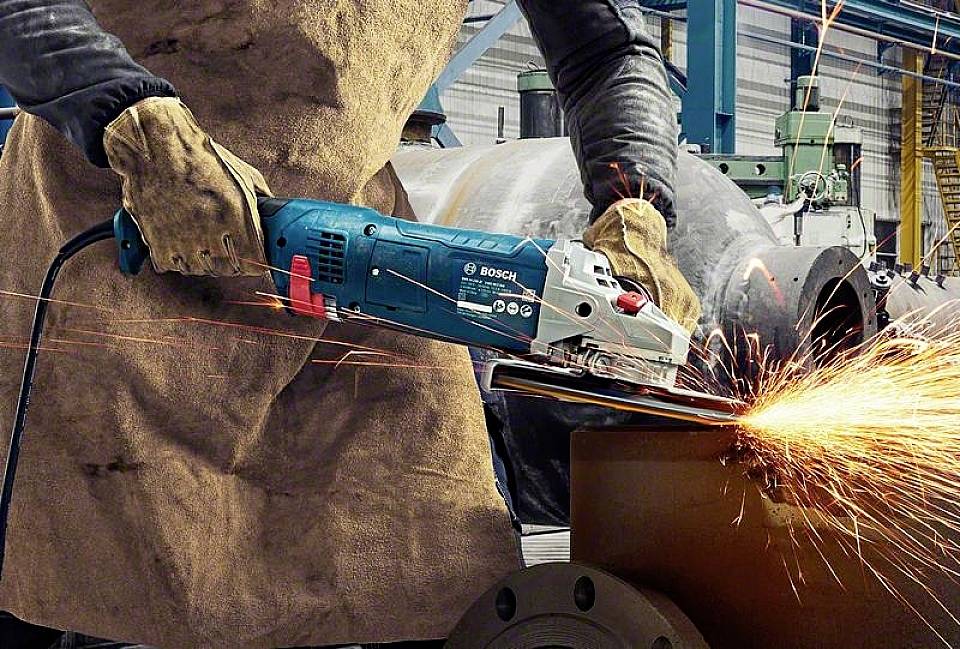 Jedna osoba brusi metal kutnom brusilicom. Varnice lete. Zaštitna oprema: rukavice i pregača. Industrijski okoliš.