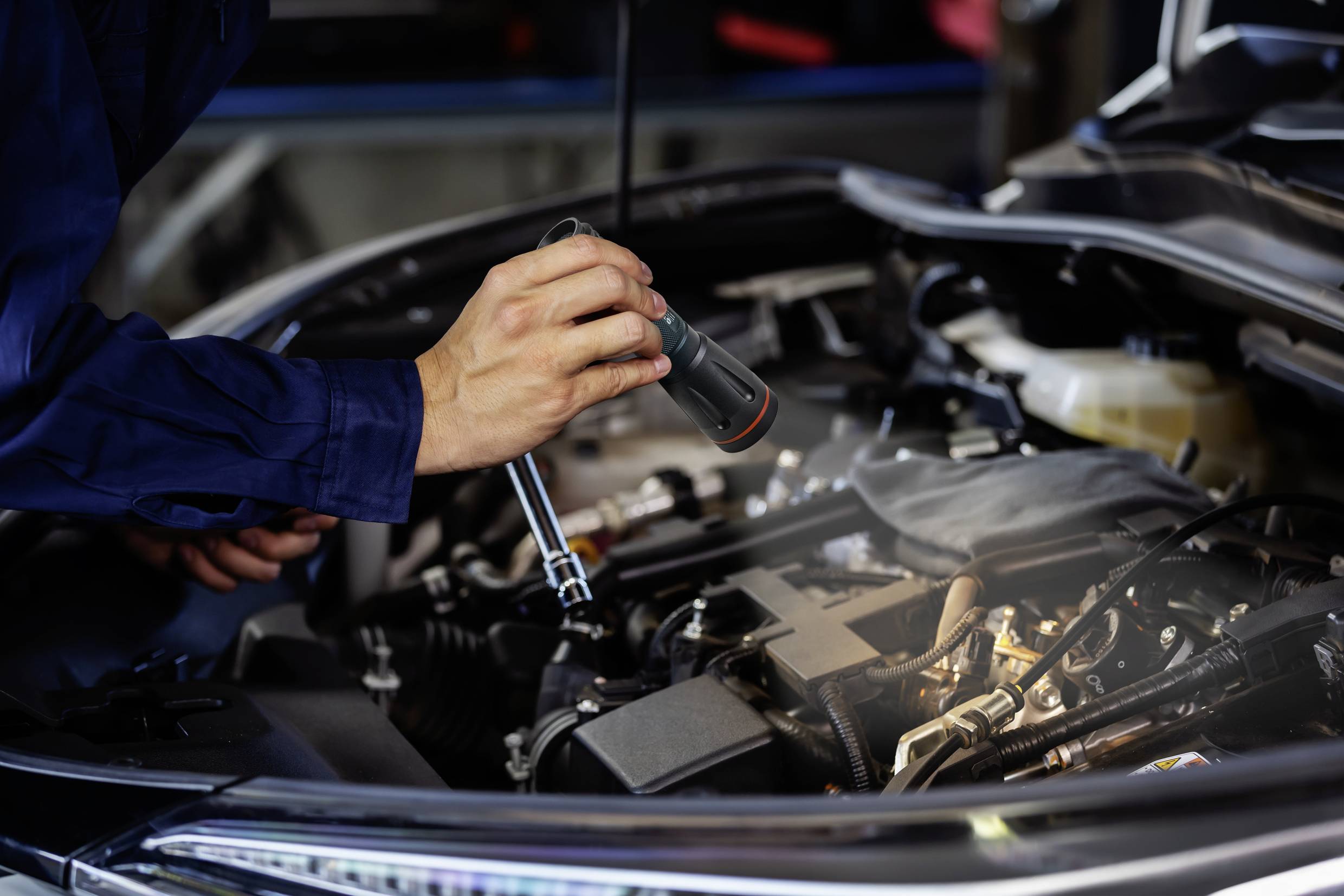 Mehaničar provjerava motor automobila džepnom lampom u radionici.