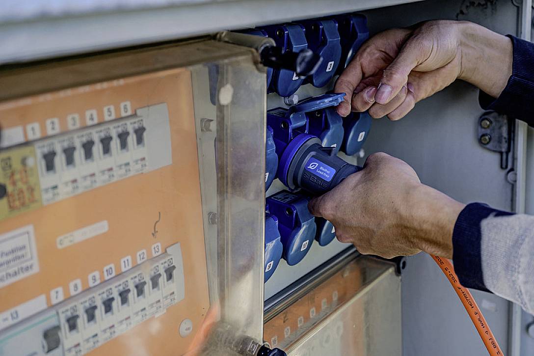 Jedna osoba uključuje plavi utikač u red utičnica u električnoj razvodnoj kutiji.