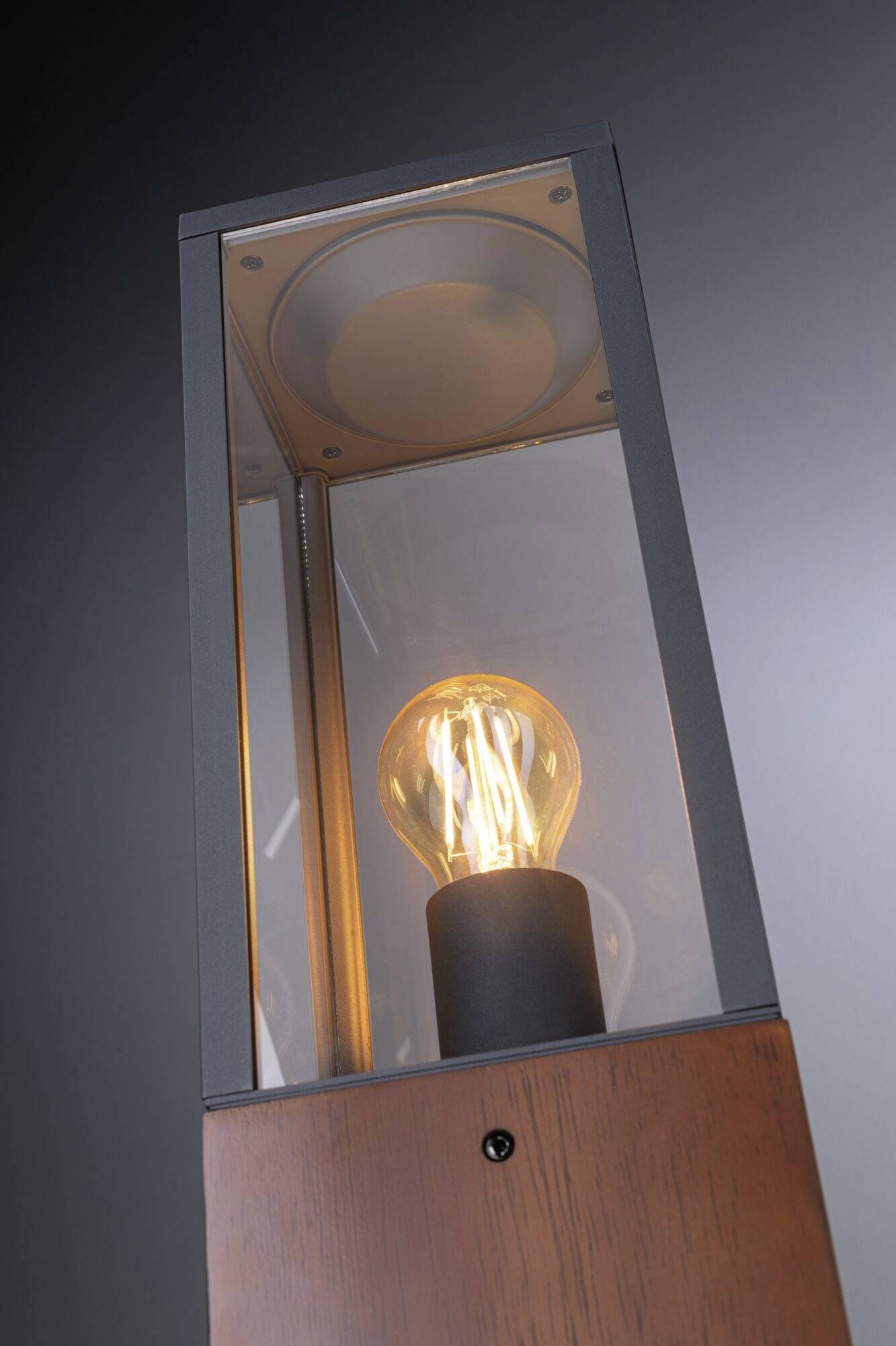 Moderna lampa sa vidljivom žaruljom unutar pravokutnog staklenog okvira na tamnoj pozadini.