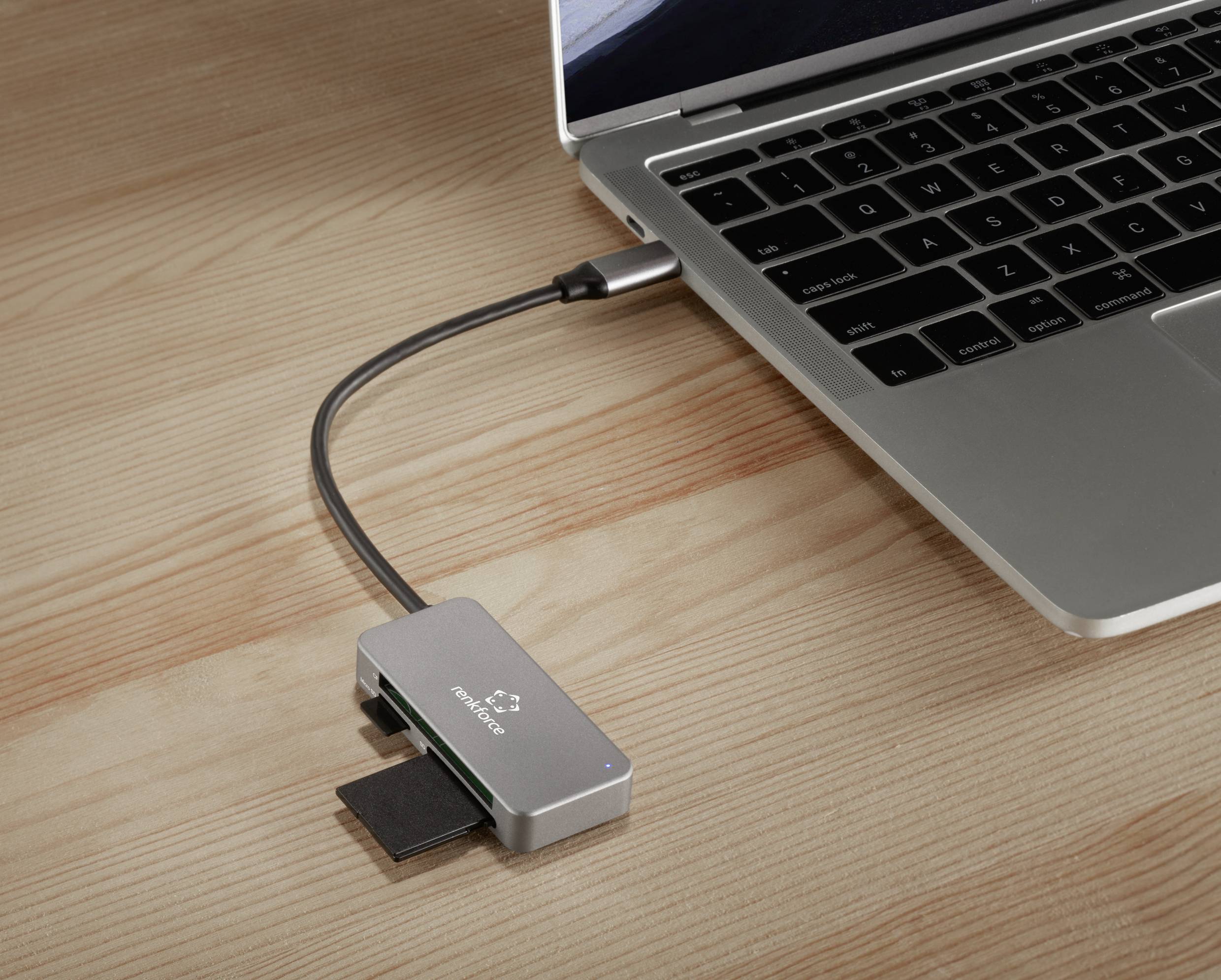 Prijenosno računalo povezano je putem USB-C razvodnika s više priključaka, uključujući onaj za SD kartice. Postav se nalazi na drvenom stolu.