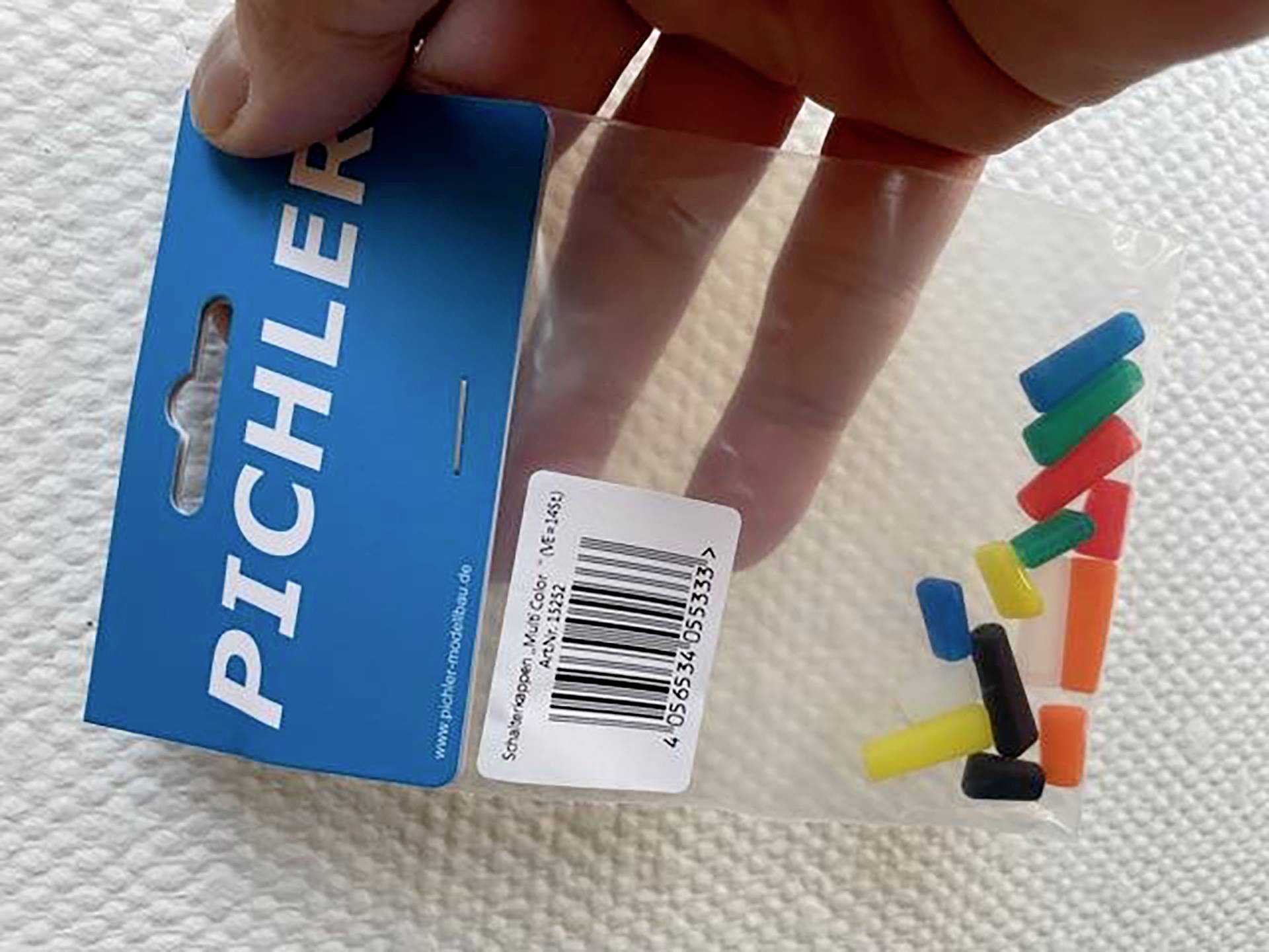 Ruka drži plastičnu ambalažu koja sadrži male, šarene, cjevaste dijelove. Na plavoj ambalaži piše 'Pichler'.